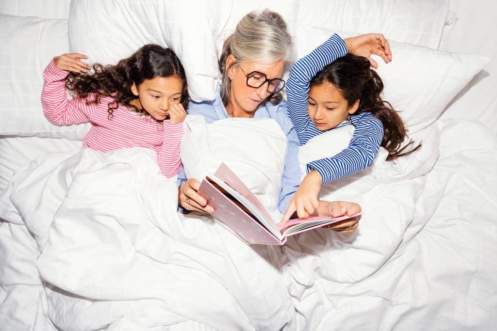 Grandmother and grandkids lying in bed reading a book together