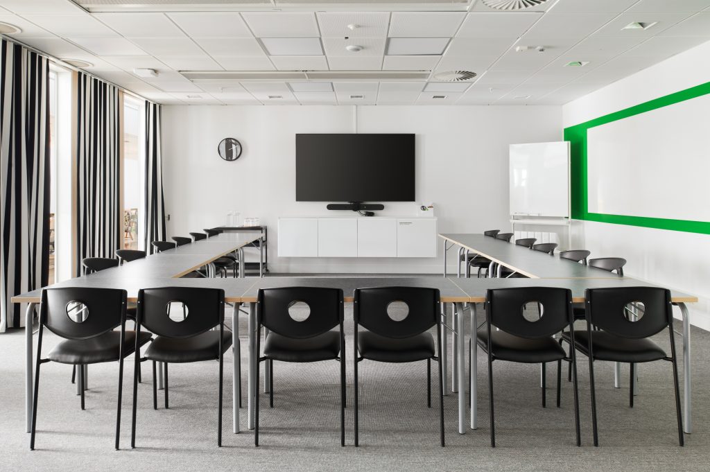 A conference room with green details and striped curtains. Chairs and tables lined up in a