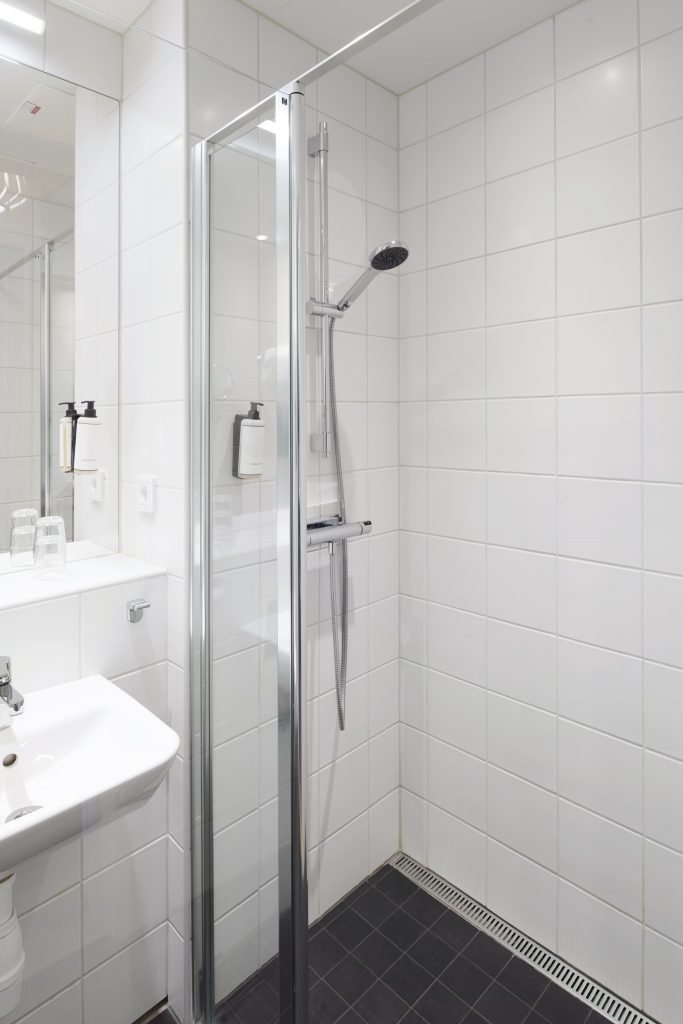 En dusch i ett badrum med glasväggar och med duschtvål bredvid duschmunstycket.