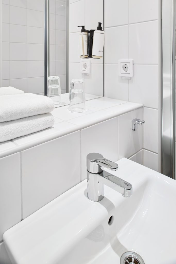 Ett tvättställ i ett badrum med ihopvikta handdukar, vattenglas och handtvål bredvid.