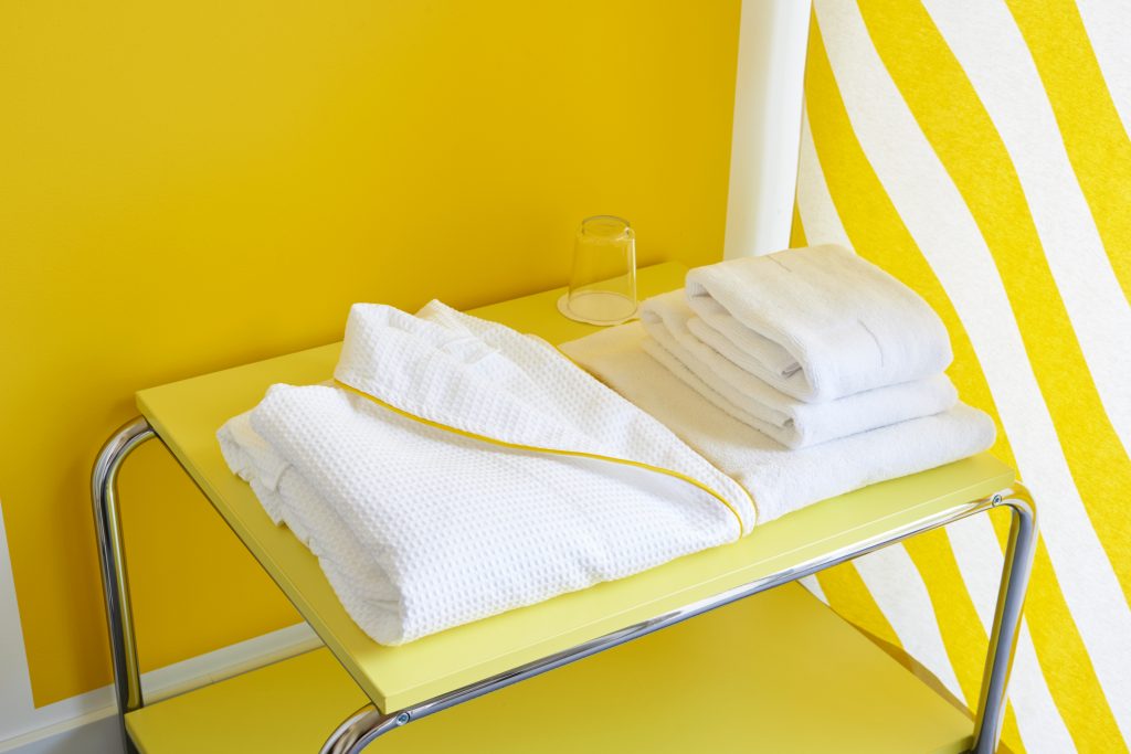 En vit badrock med gula detaljer och handdukar som ligger på ett gult nattduksbord.