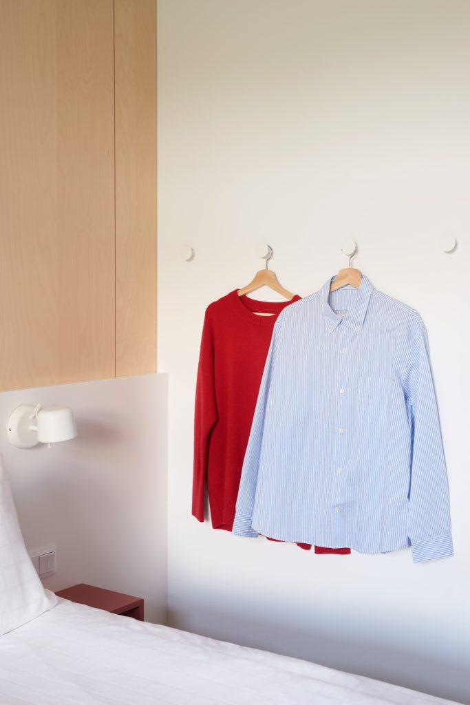 Klädesplagg som hänger på krokar bredvid en dubbelsäng.