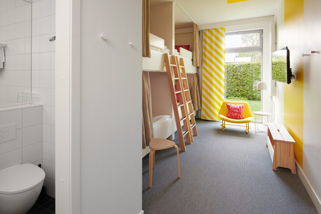 En vy över ett familjerum, med TV, fyra platsbyggda sängar, en fåtölj och öppen dörr till badrummet.